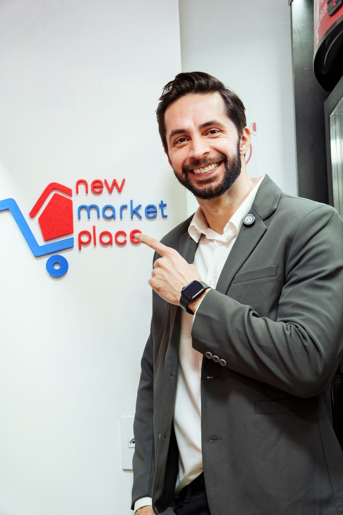 Executivo da New Market Place, de terno, sorri e aponta para o logotipo aplicado na parede da loja