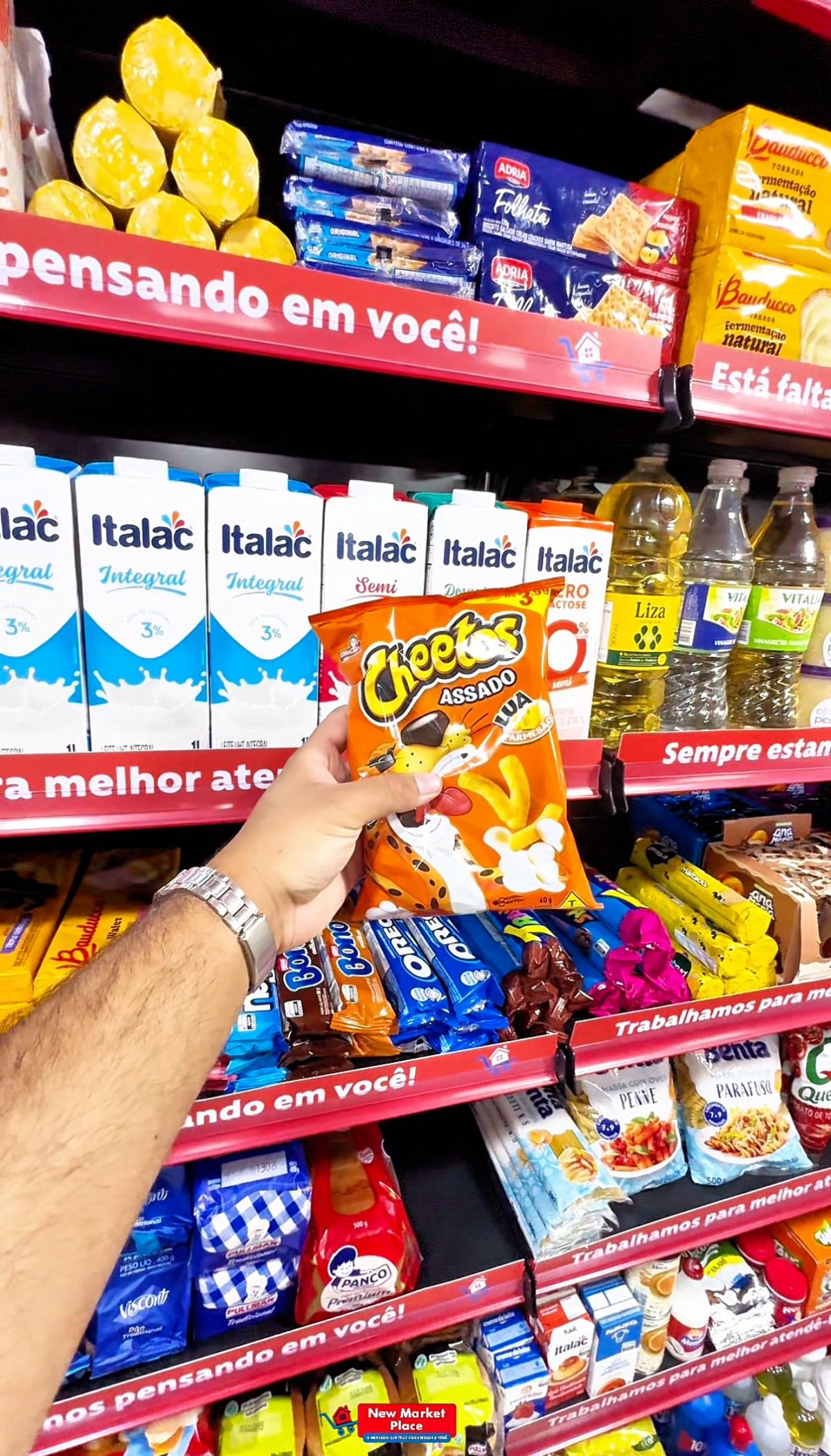 Mão segura um salgadinho em frente à prateleira de leite e biscoitos